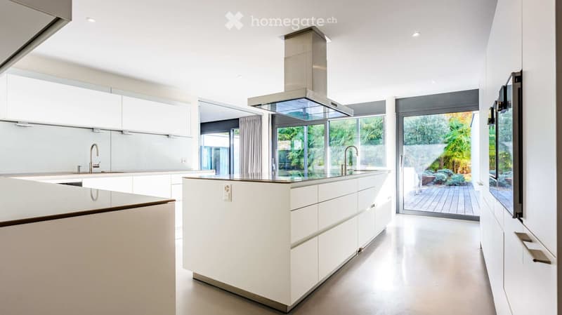 Modern, minimalist kitchen with white cabinets, a central island, and large windows offering a view of the garden.