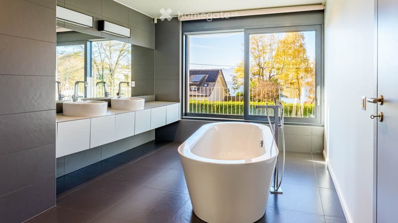Modern bathroom with a freestanding bathtub, double sink vanity, large mirror, and expansive windows offering a scenic view.