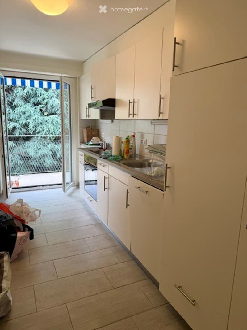 Modern kitchen with white cabinets, stainless steel appliances, and a large window leading to a balcony.