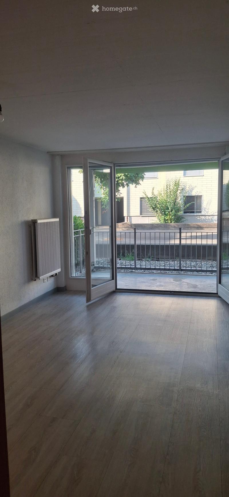 Empty room with wooden flooring, white walls, and large sliding glass doors leading to a balcony area with a metal railing and outdoor space.