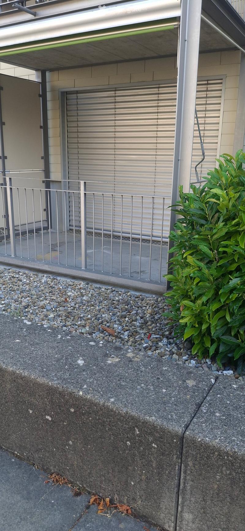 A small outdoor area with a metal railing, a closed garage door, and a small patch of gravel and greenery.
