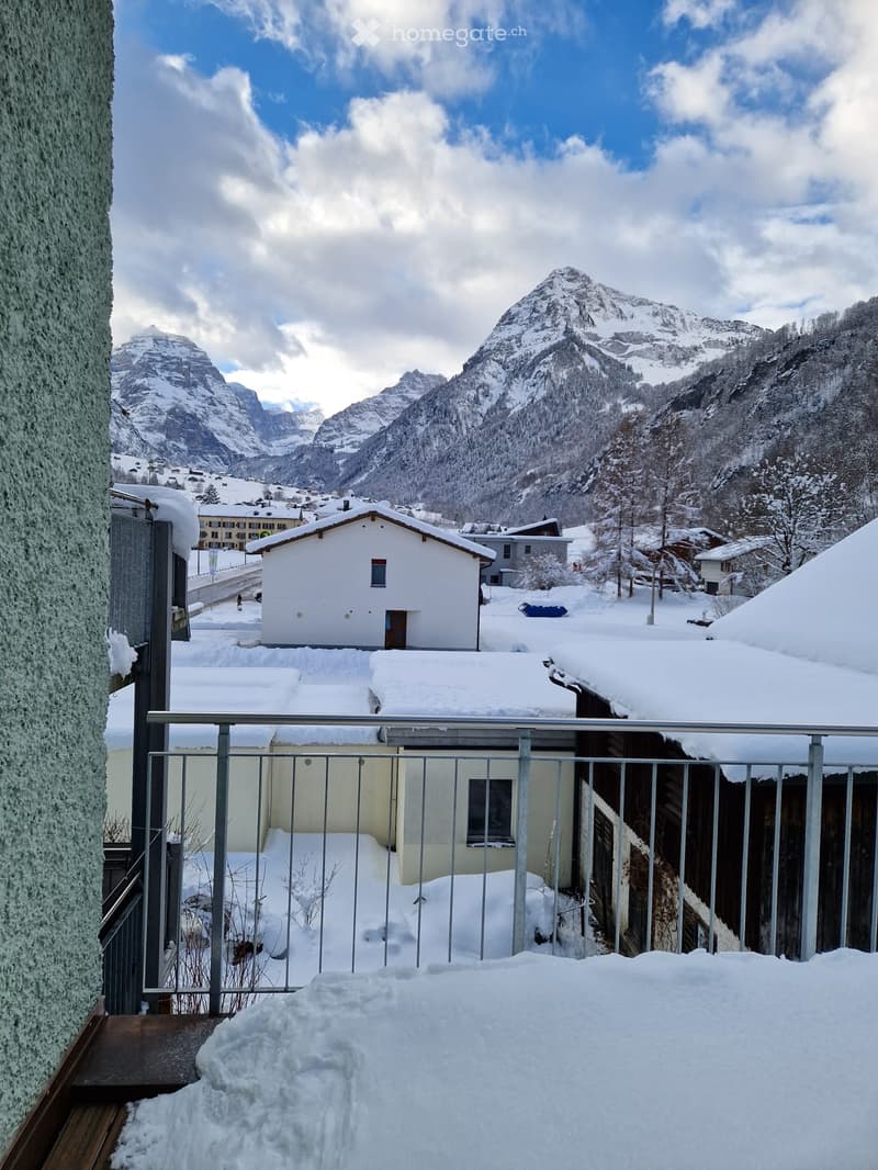 Balcony overlooking a snowy village with snow-covered mountains in the background.