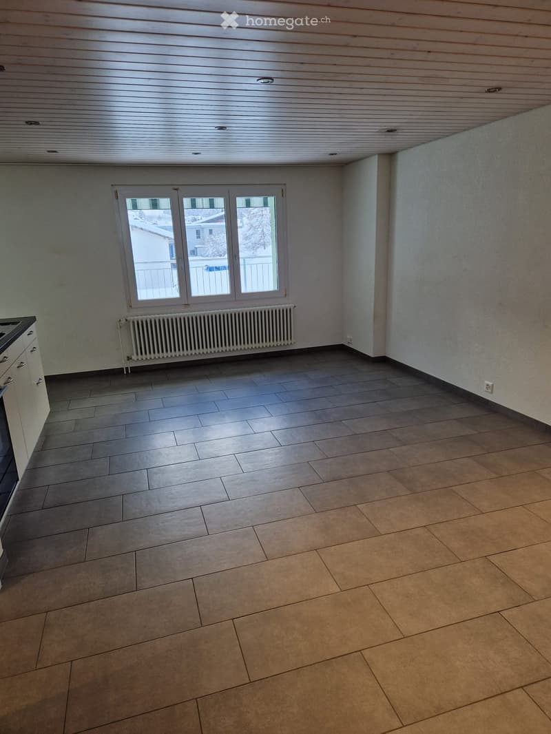Large empty room with wooden tiles, windows, and a white radiator.