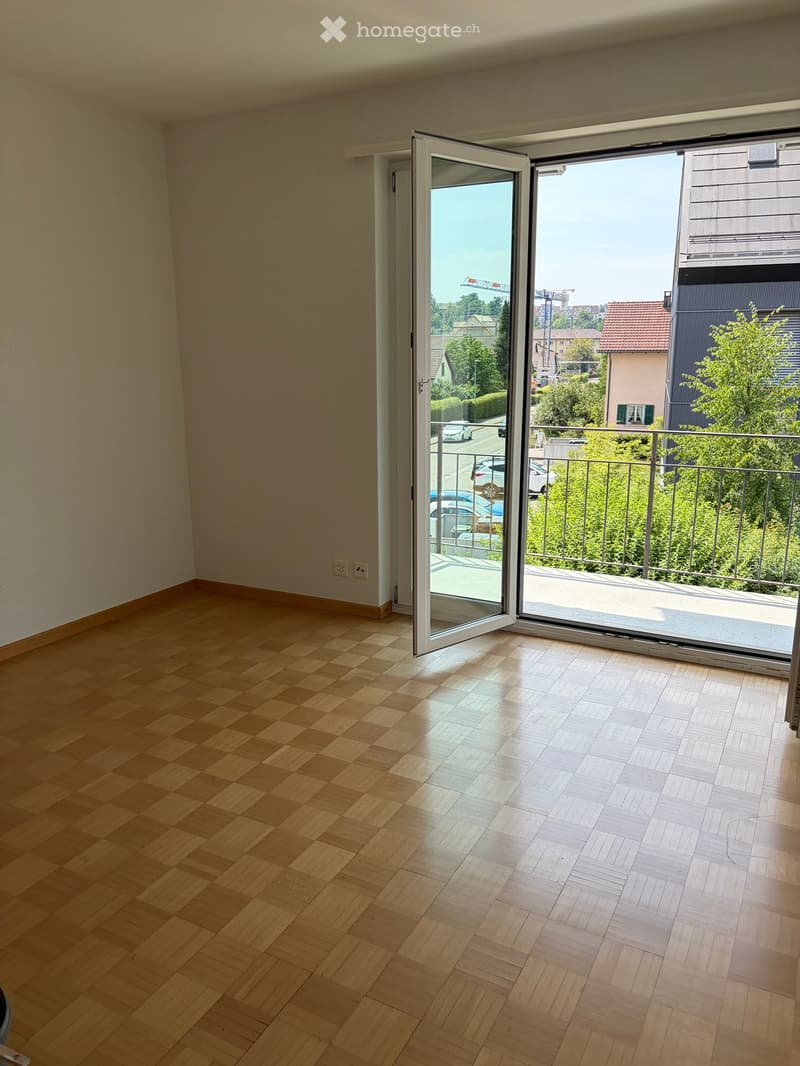 Empty room with wooden flooring and large sliding glass doors leading to a balcony with a metal railing.