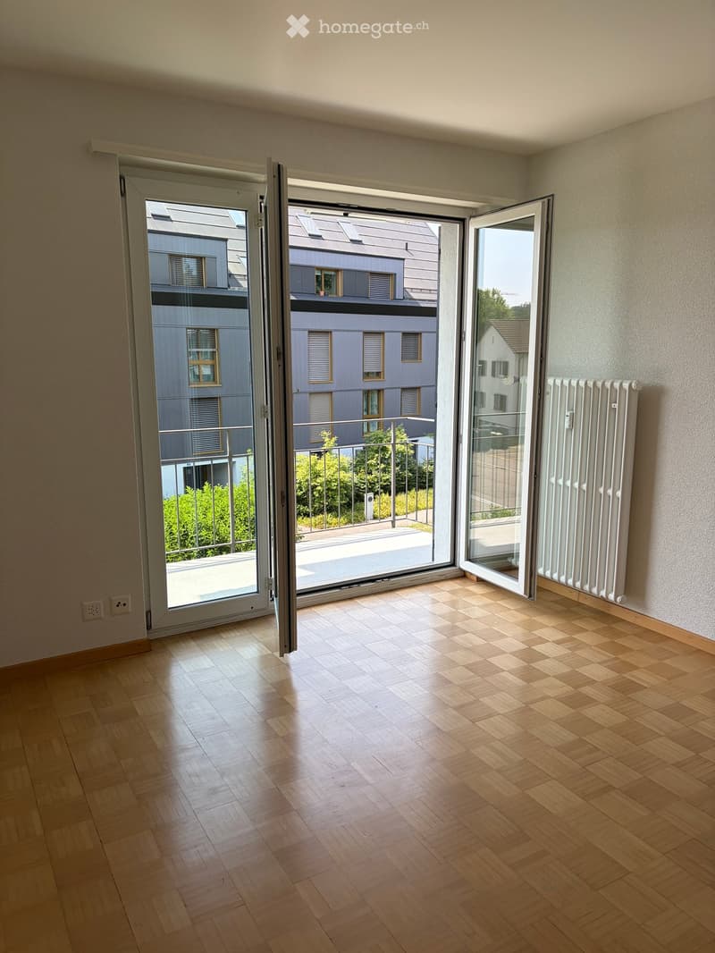 Empty room with wooden flooring, large sliding glass doors leading to a balcony, radiator on the wall, and visible electrical outlets.