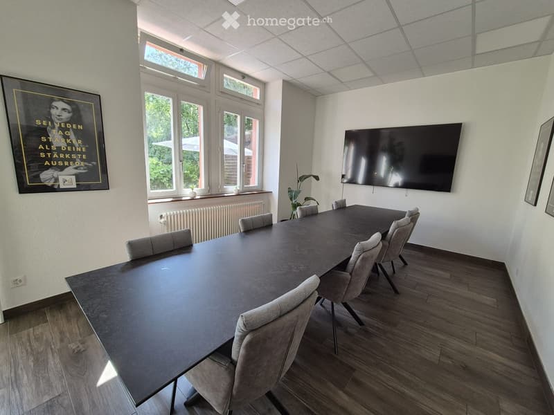 Conference room with a long table, chairs, a large screen, and a picture frame on the wall. The room has large windows and a modern design.