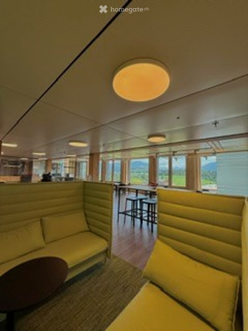 Modern lounge area with yellow upholstered seating, round wooden table, and large windows offering a scenic ocean view.