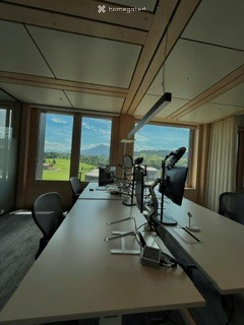 Bright, modern meeting room with large windows, a long wooden table, several chairs, laptops, and a screen for presentations.