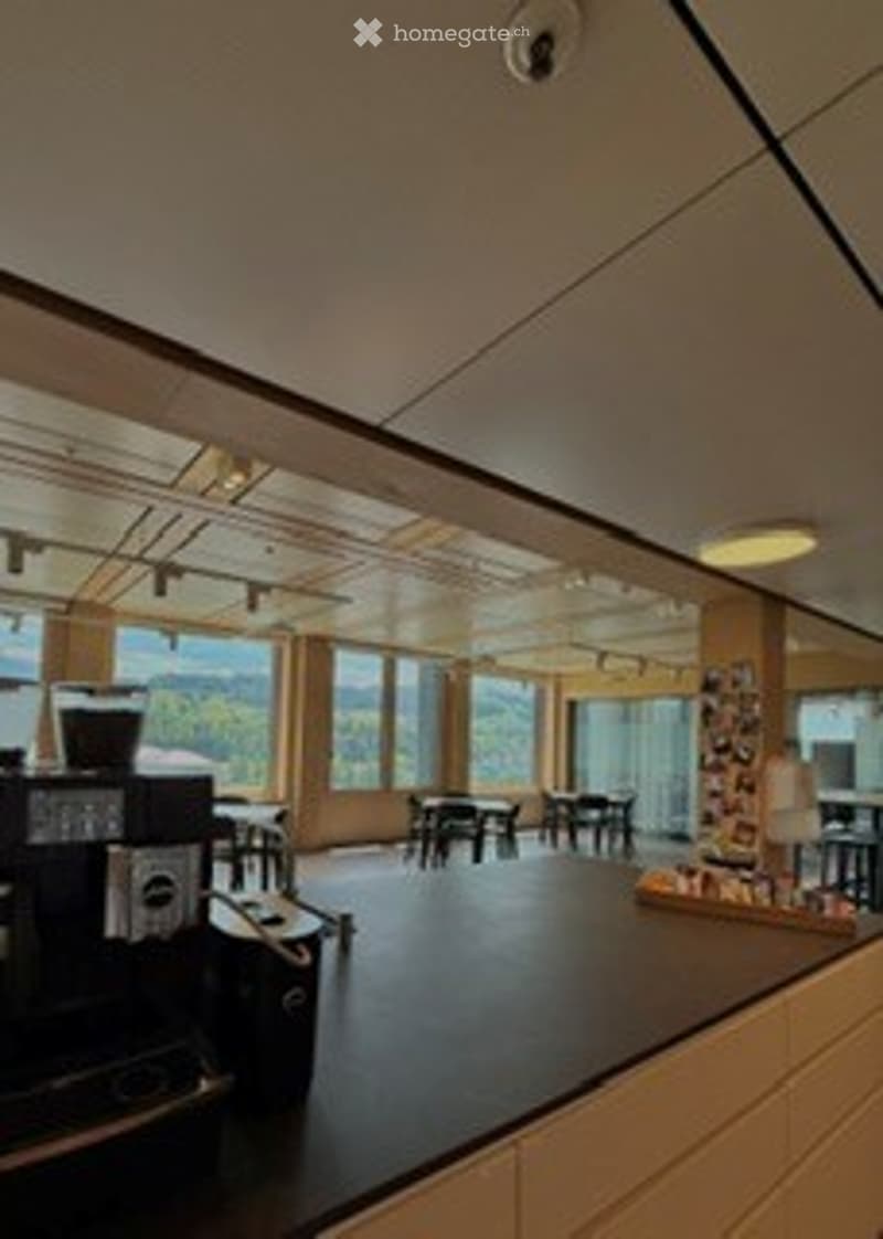 Modern kitchen with large windows, black countertops, coffee machine, and several tables and chairs.