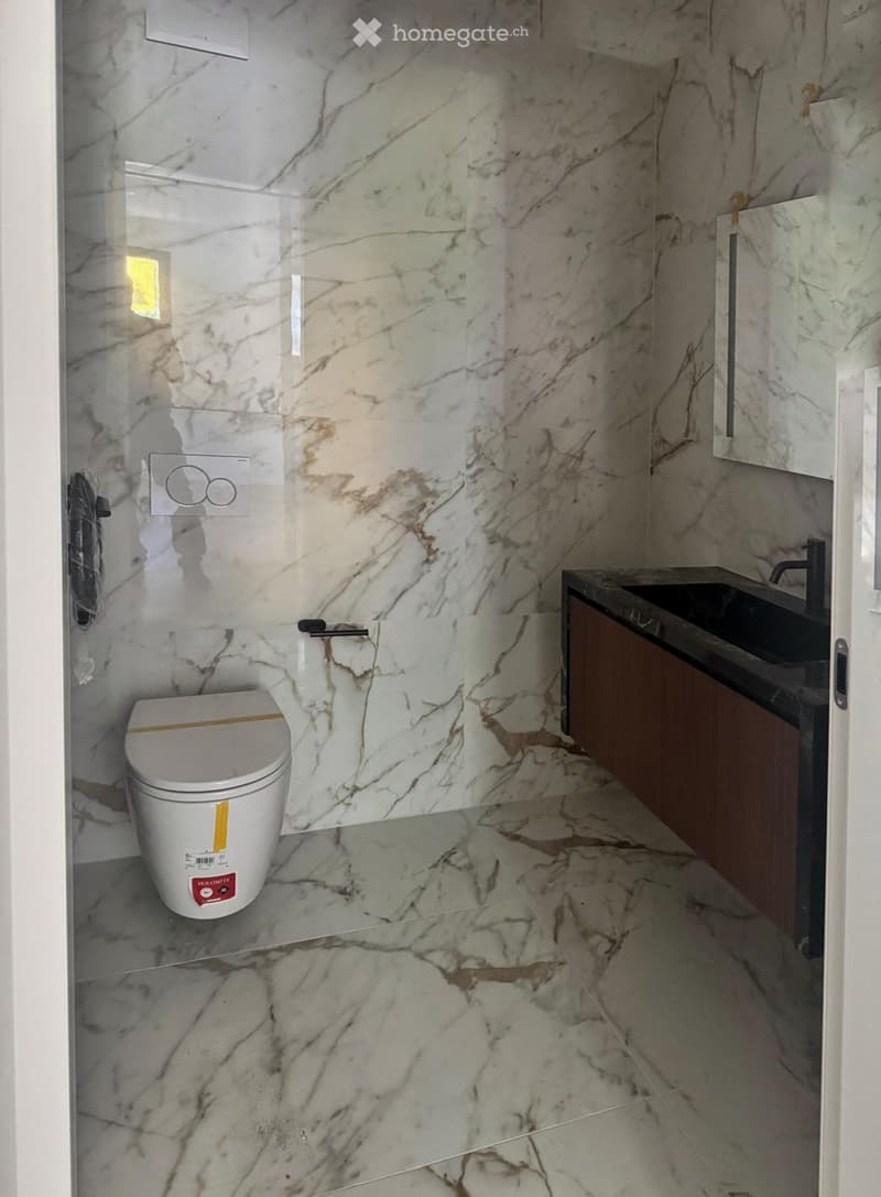 Modern bathroom with marble walls and floor, featuring a toilet, sink, and wooden cabinet.
