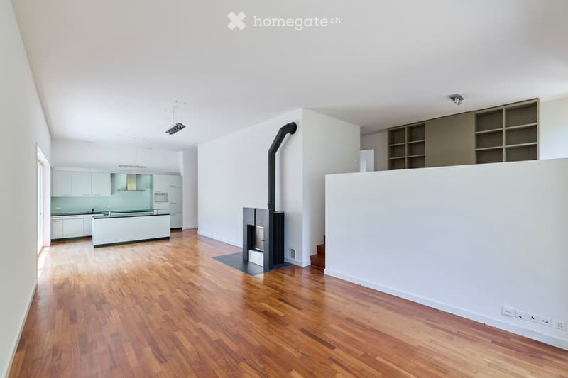 Open-plan living and kitchen area with wooden flooring, modern kitchen cabinets, a central island, and a fireplace with a chimney.