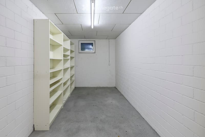 Empty room with white brick walls, concrete floor, and a single white shelving unit against one wall. A small window is visible on the opposite wall.