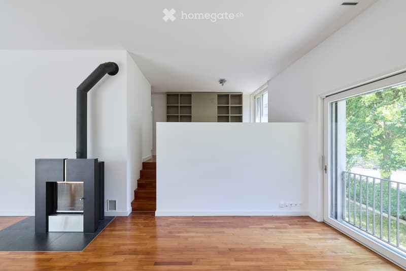Modern living room with a sleek, grey fireplace, built-in shelving unit, large windows, and wooden flooring.