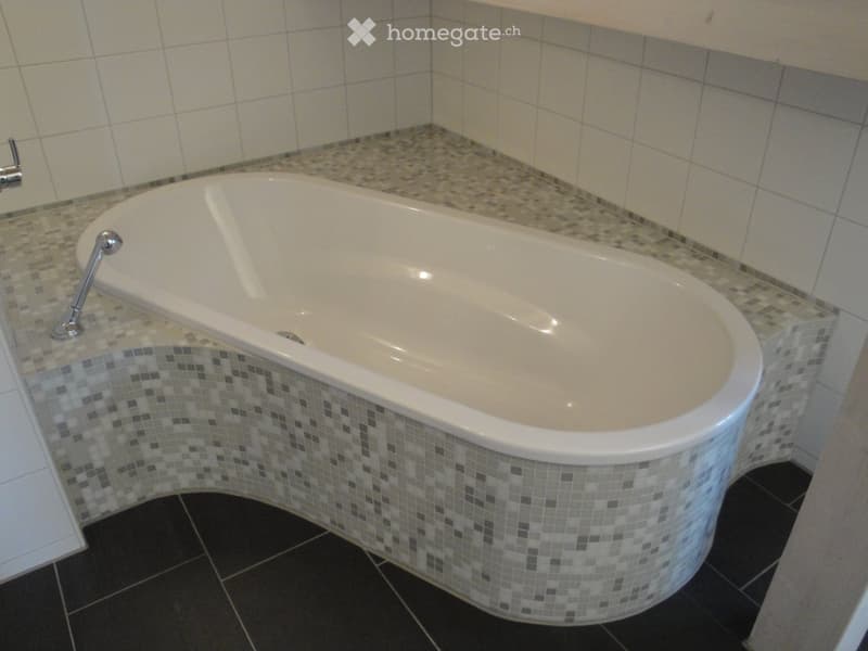 Modern bathroom with a large, corner bathtub featuring mosaic tile accents and a sleek chrome faucet.