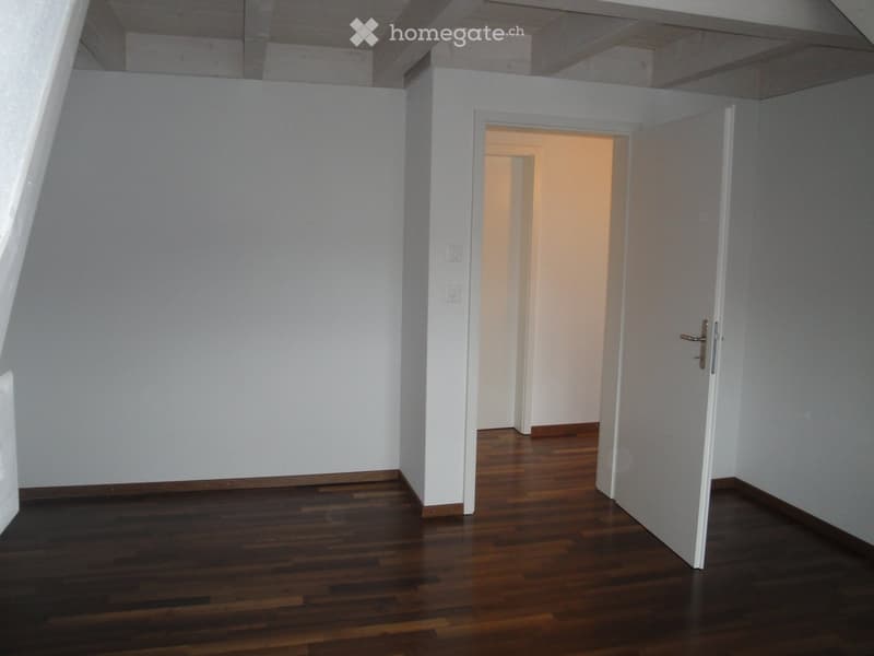 Empty room with wooden flooring and white walls, featuring an open doorway leading to another room.