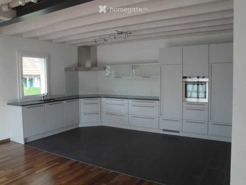 Modern kitchen with grey cabinets, stainless steel appliances, black countertop, and dark tiled floor.
