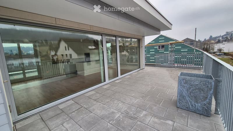 Modern balcony with large glass sliding doors, tiled floor, and a decorative stone planter.