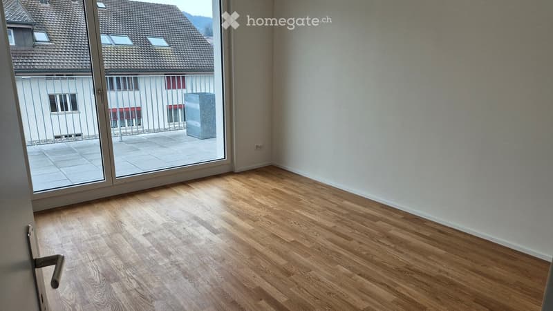 Empty room with wooden flooring and large sliding glass door leading to a balcony area.