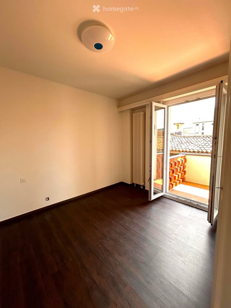 Empty room with wooden flooring, white walls, and an open sliding door leading to a balcony or terrace area.