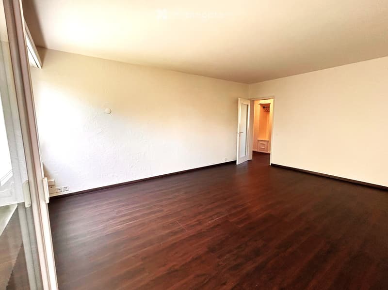 Empty room with wooden flooring and white walls, featuring a doorway leading to another room.