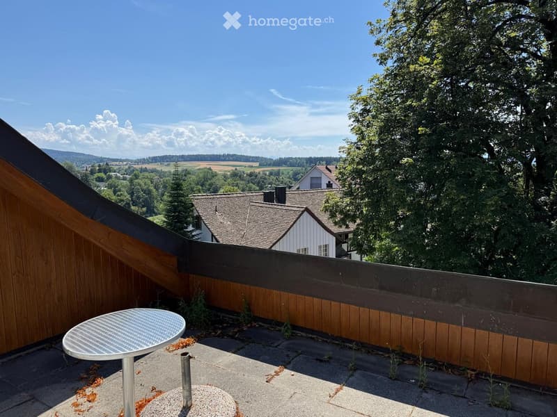 Balcony with wooden railing, metal table, and scenic countryside view.