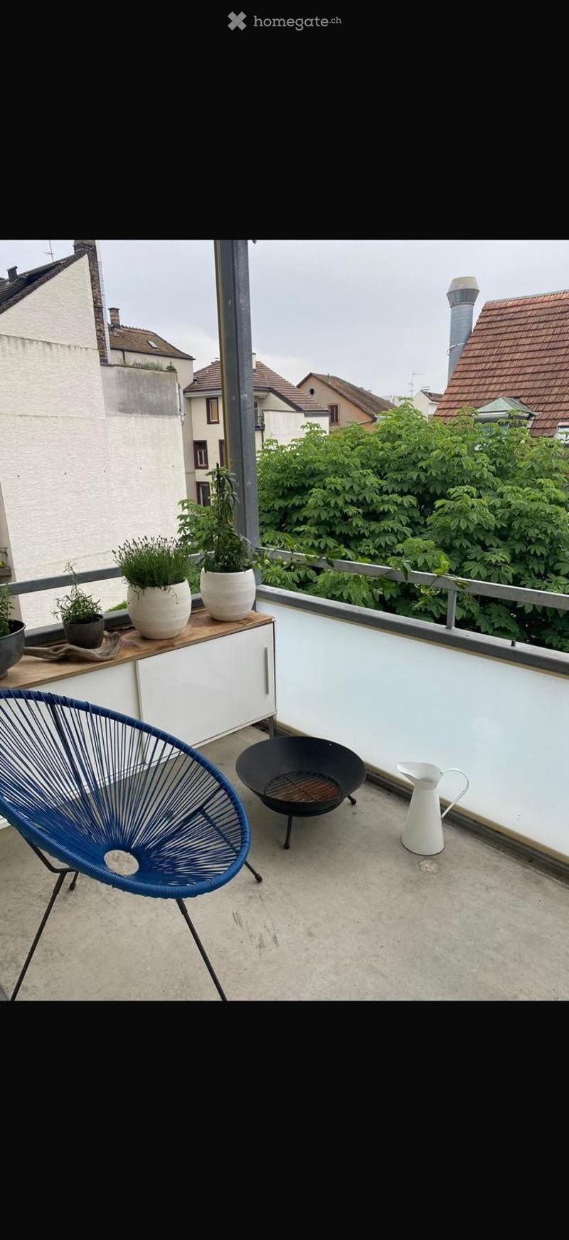 Balcony with a blue wire chair, a black fire bowl, potted plants on a small cabinet, and a white pitcher.