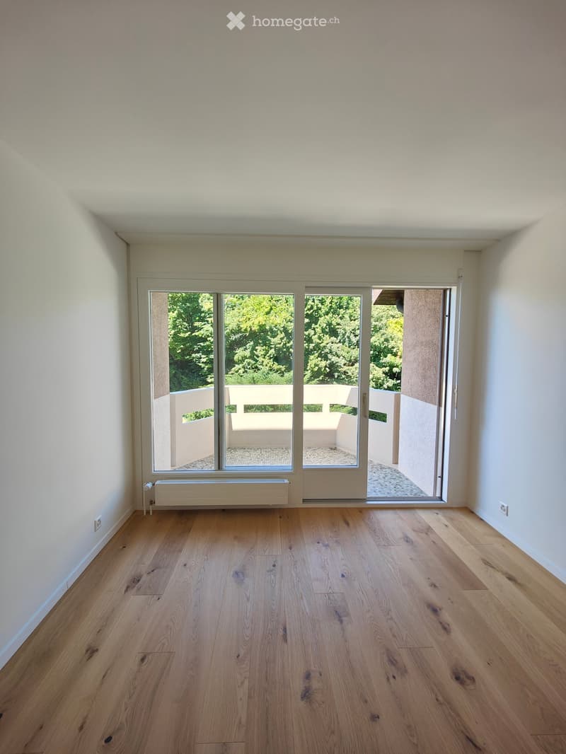 Empty room with light wooden flooring, white walls, large sliding glass doors leading to a balcony, and a radiator under the window.