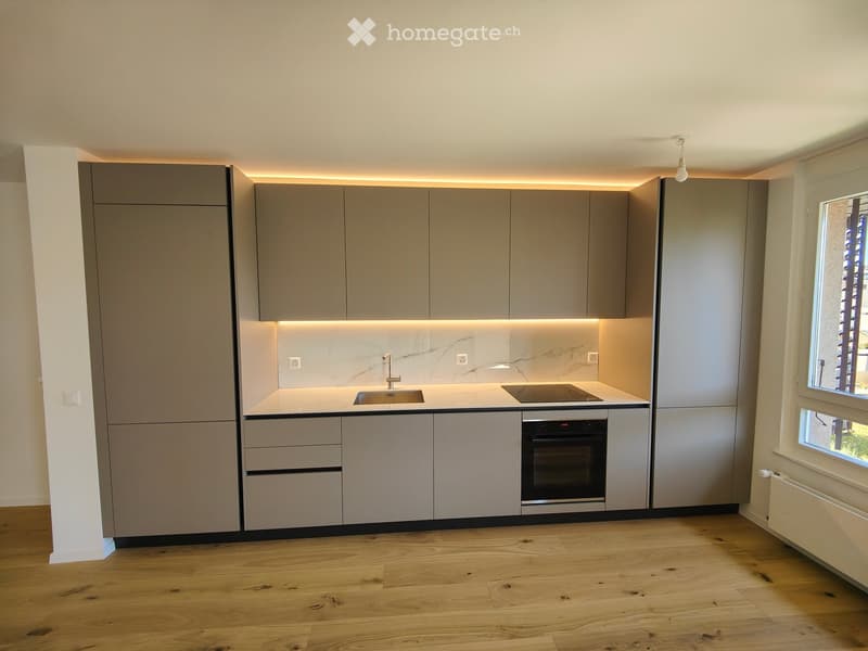 Modern kitchen with light grey cabinets, a marble backsplash, a sink, a faucet, and an oven. The floor is made of light wooden planks.