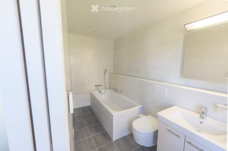 Modern bathroom with white tiles, a bathtub, toilet, sink, and a mirrored cabinet.