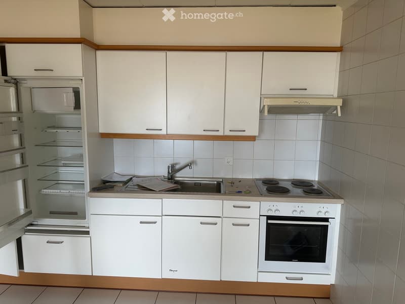 Compact kitchen with white cabinets, a refrigerator, stove, oven, and sink. Wooden trim accents the cabinetry.