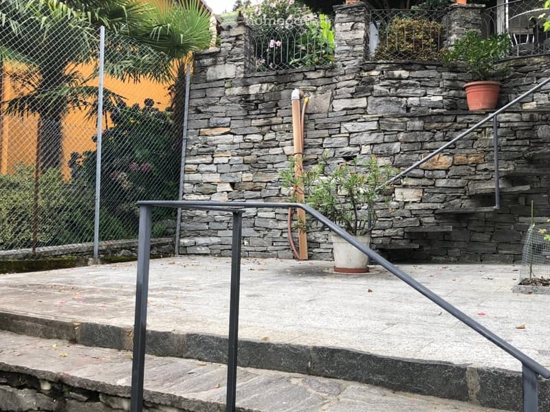 stone wall, metal railing, stairs, plants in pots, chain-link fence