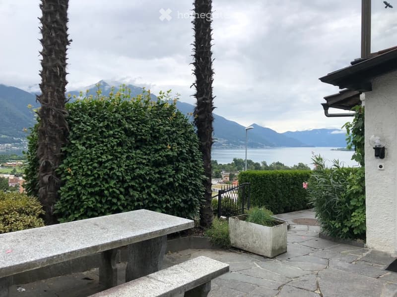 Outdoor seating area with a bench, a table, and a potted plant. View of mountains and a body of water in the background.