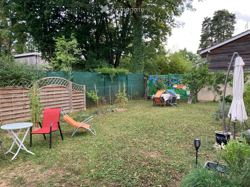 Garden with grass, wooden fence, colorful mural, outdoor furniture including a table, chairs, and an umbrella.