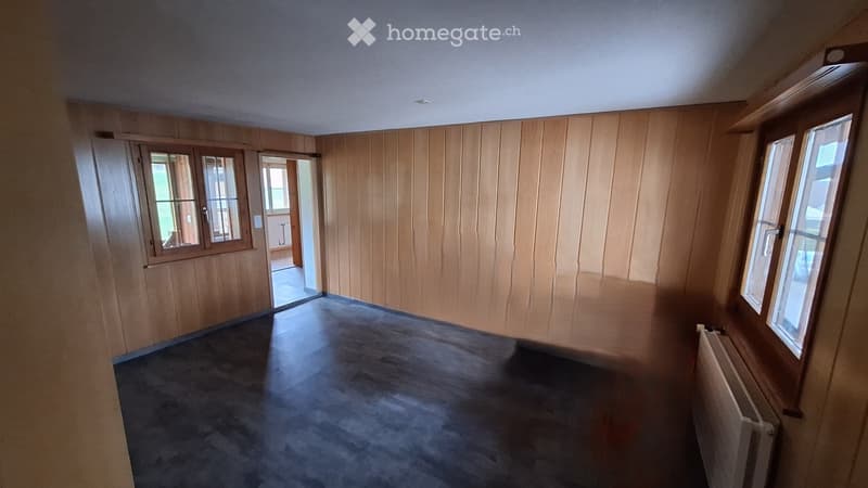 Empty room with wooden panel walls, carpeted floor, and large windows. No furniture or equipment present.