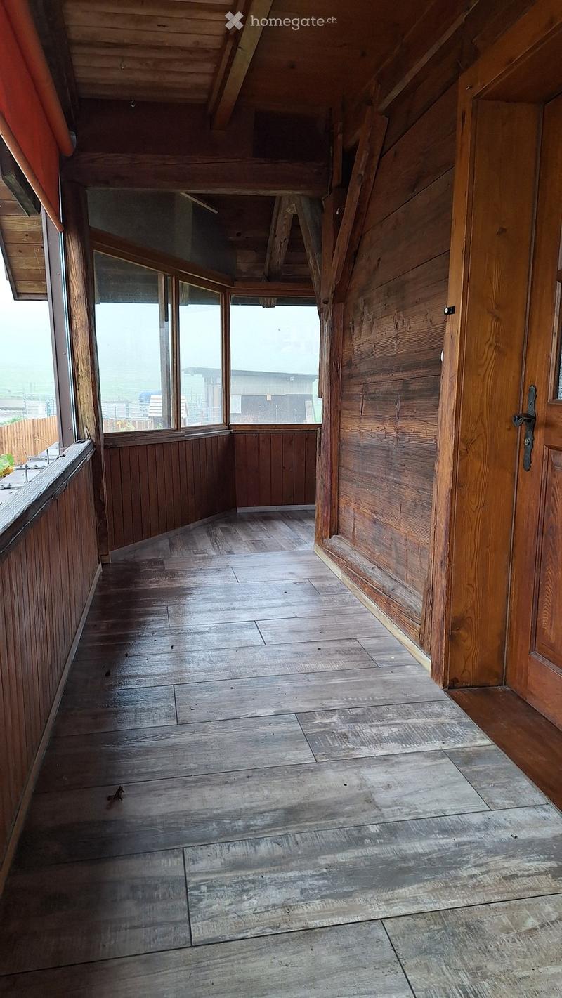 Empty wooden hallway with exposed beams, large windows, and a mix of wooden and concrete flooring.