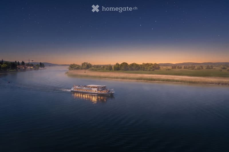 A serene river scene at sunset with a boat gliding on calm waters, surrounded by lush greenery and distant hills under a starry sky.