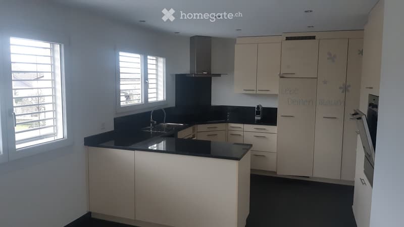 Modern kitchen with white cabinets, black countertops, and a central island. Features a stainless steel range hood, sink, and faucet.