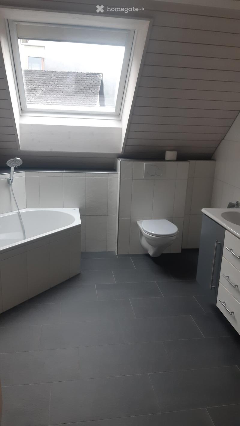Modern bathroom with dark grey tiles, a bathtub, toilet, sink, and a skylight window above.