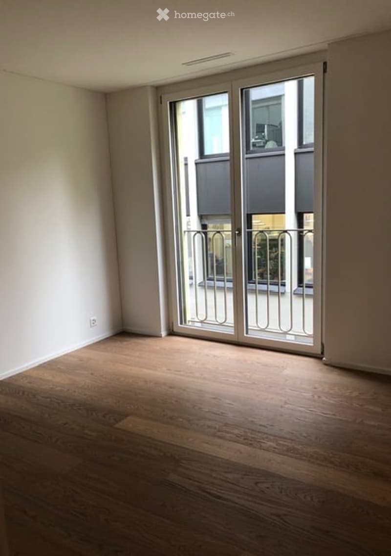 Empty room with wooden flooring and large glass sliding doors leading to a balcony area.