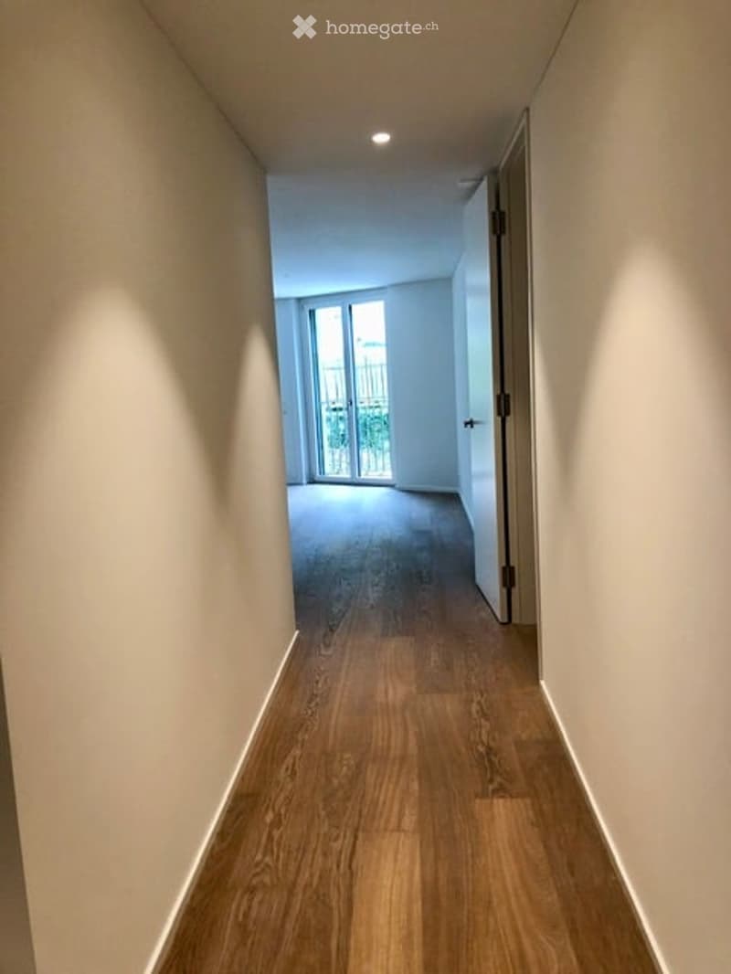 Empty hallway with wooden flooring, white walls, and a door leading to a balcony or terrace area.