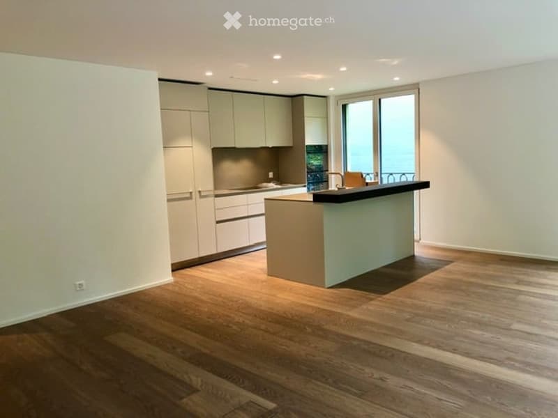 Modern kitchen with light-colored cabinets, a central island, and a large window offering a view of the balcony.