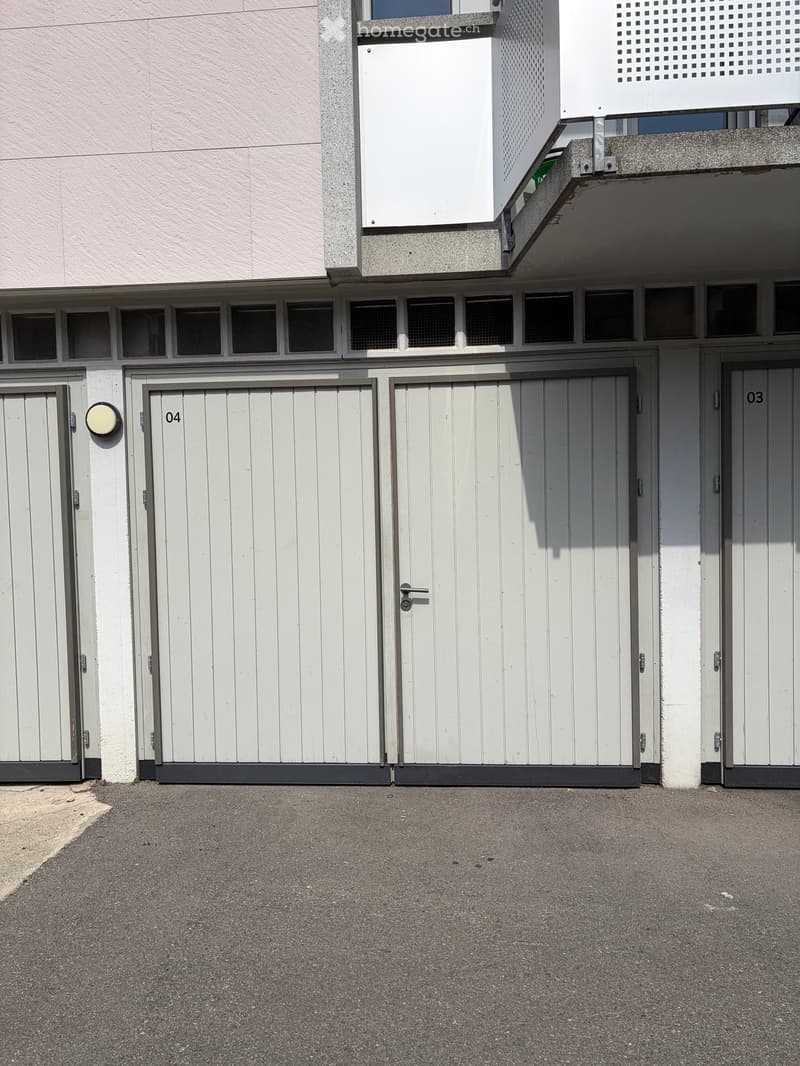 Exterior view of a building with multiple garage doors, numbered 03, 04, and others, and a small balcony area above.