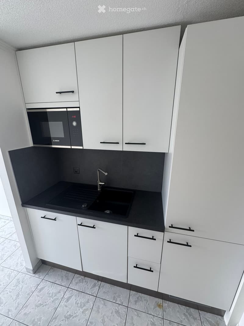 Modern kitchen with white cabinets, black countertop, stainless steel sink, and microwave.