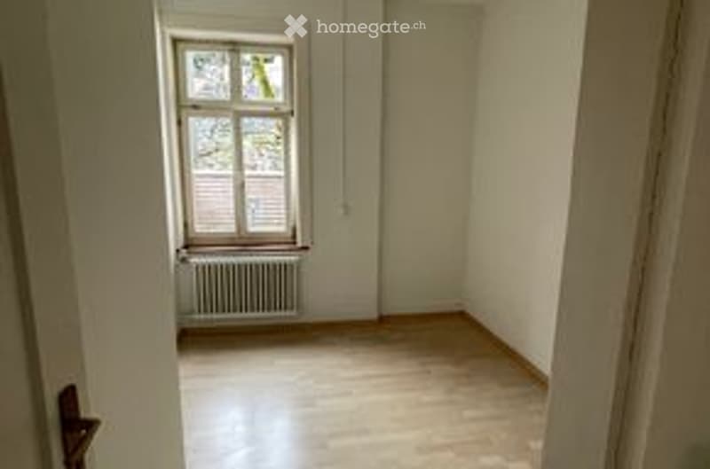 Empty room with wooden flooring, white walls, and a single window with a radiator below it. No furniture or equipment present.