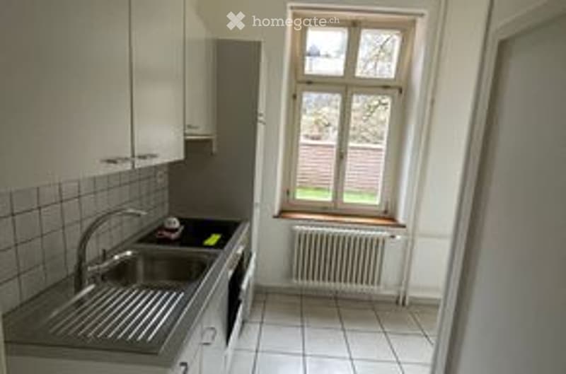 Modern kitchen with white cabinets, stainless steel sink, radiator, and tiled walls.