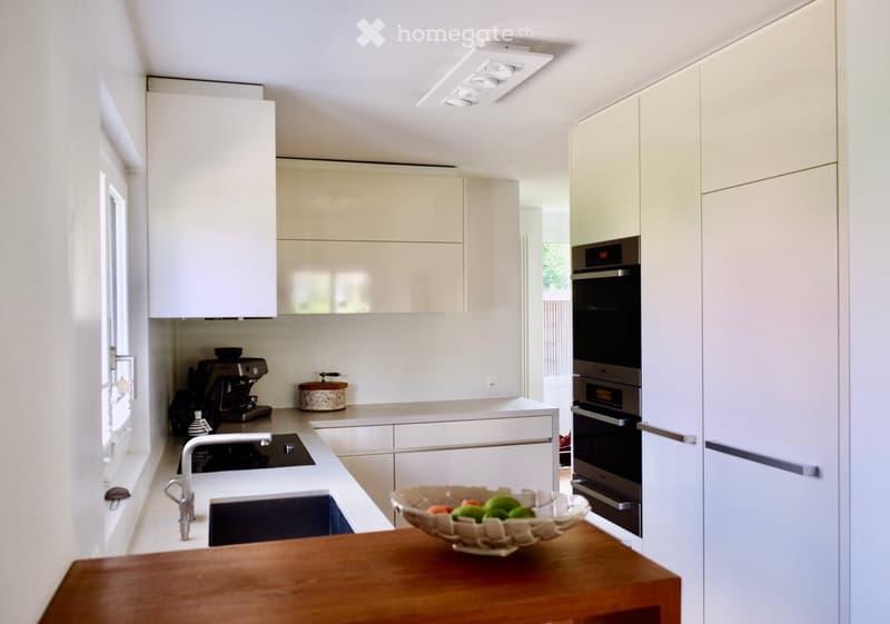 Modern kitchen with white cabinets, stainless steel appliances, a wooden table, and a bowl of fruit on the counter.