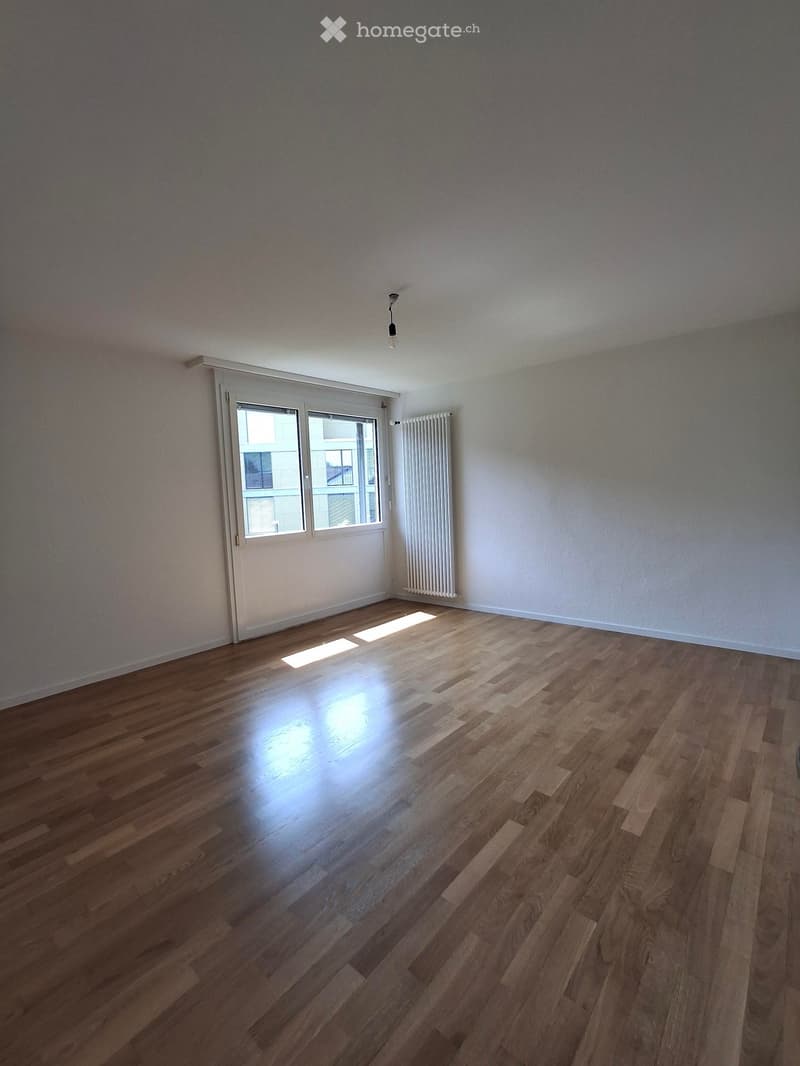 Empty room with wooden flooring, white walls, a radiator, and a sliding glass door leading to a balcony.
