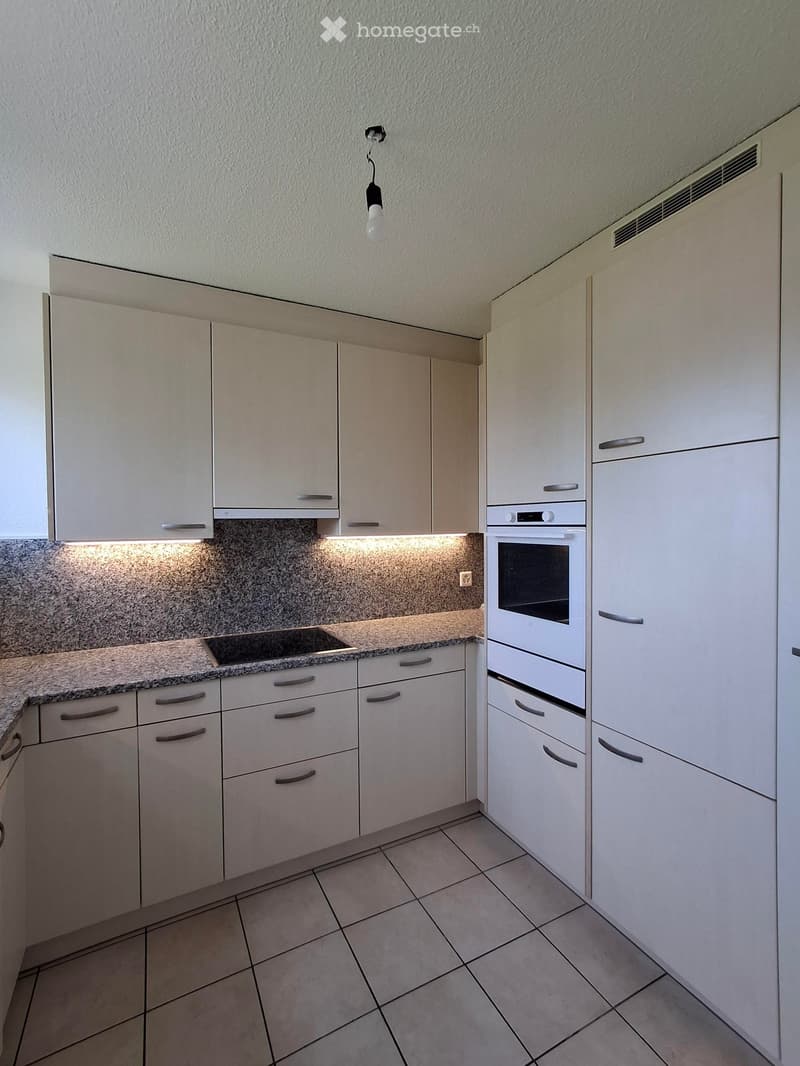 Modern kitchen with white cabinets, granite countertop, built-in oven, and tiled floor.