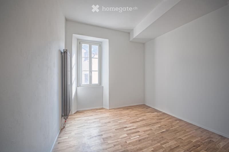 Empty room with light-colored wooden flooring, white walls, and a single window with white frame and glass panes.