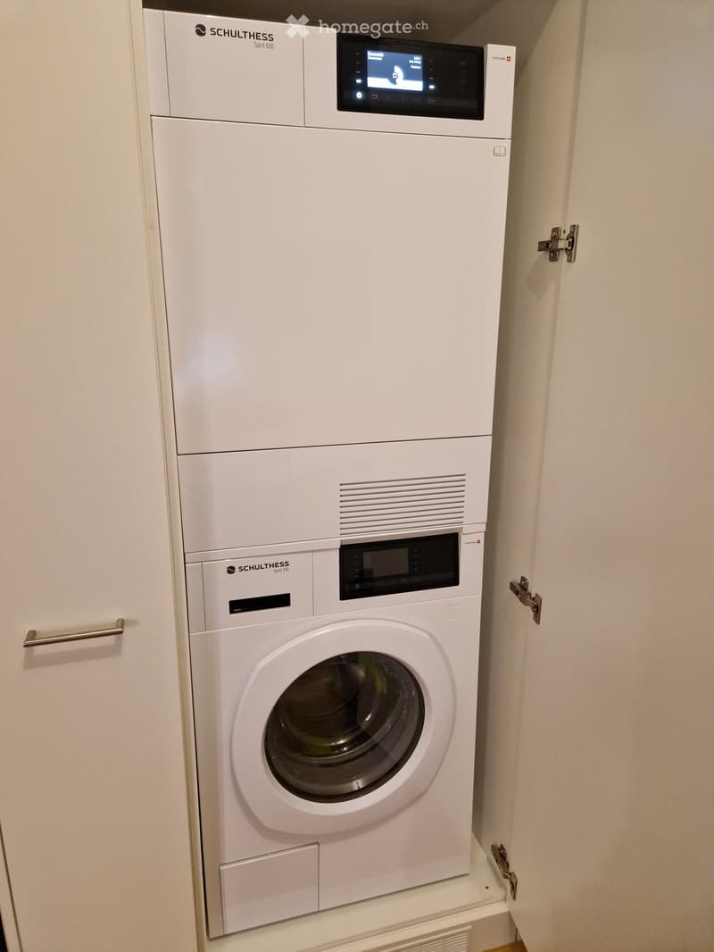 A compact bathroom with a white washing machine and a white dishwasher stacked vertically, both featuring digital displays and control panels.